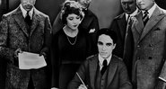 Chaplin sentado e assinando o documento da fundação da United Artists - Wikimedia Commons