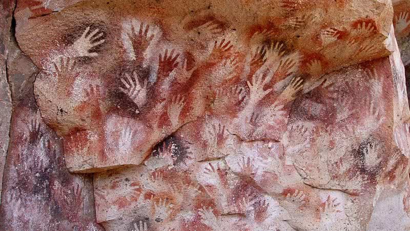 Pintura rupestre de mãos na famosa "Caverna de Las Manos" - Domínio Público