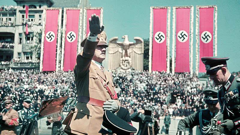 Adolf Hitler saudando seus membros, cercado por símbolos nazistas