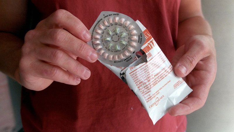Imagem ilustrativa de mulher segurando cartela de anticoncepcionais - Getty Images