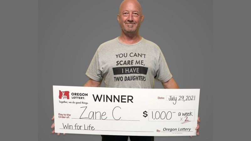 Zane segura um dos cheques ilustrativos que asseguram o prêmio - Divulgação / Loteria Estadual de Oregon