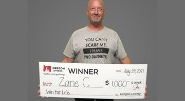 Zane segura um dos cheques ilustrativos que asseguram o prêmio - Divulgação / Loteria Estadual de Oregon