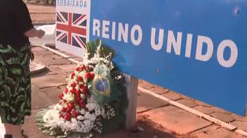 Imagem de mulher em frente à embaixada com flores e uma bandeira do Brasil - Reprodução/Vídeo/G1