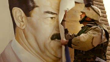 Militar estadunidense removendo cartaz com rosto de Saddam Hussein, durante a Guerra do Iraque - Getty Images