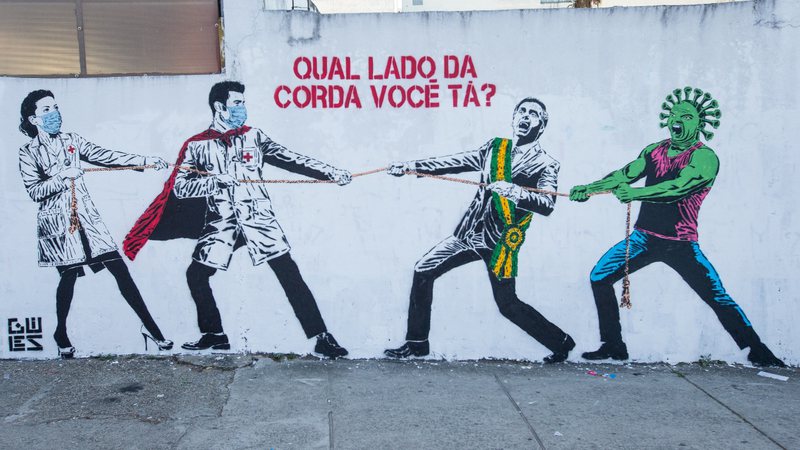 Grafite representando Jair Bolsonaro e o coronavírus em um cabo de guerra contra os trabalhadores da saúde
