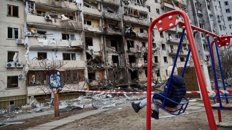 Fotografia mostrando criança se balançando em área destruída da Ucrânia - Getty Images