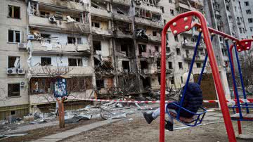 Fotografia mostrando criança se balançando em área destruída da Ucrânia - Getty Images