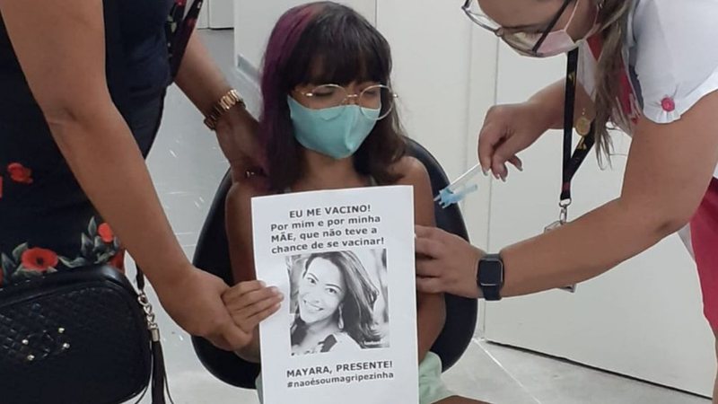 Menina segura cartaz com foto da mãe no momento da vacinação