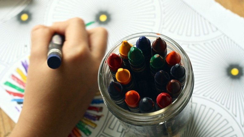 Na imagem ilustrativa, criança pinta desenho com giz de cera
