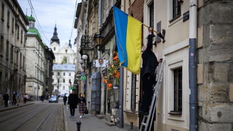 Homem coloca bandeira ucraniana em fachada de construção em Lviv