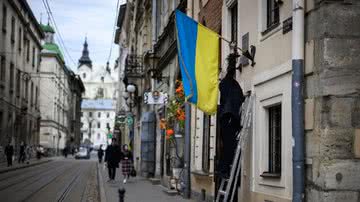 Homem coloca bandeira ucraniana em fachada de construção em Lviv - Getty Images