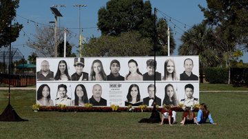 Grupo reunido em frente a painel com fotos das 17 vítimas do atentado - Getty Images