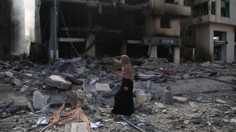 Moradora da Faixa de Gaza andando sob escombros - Getty Images