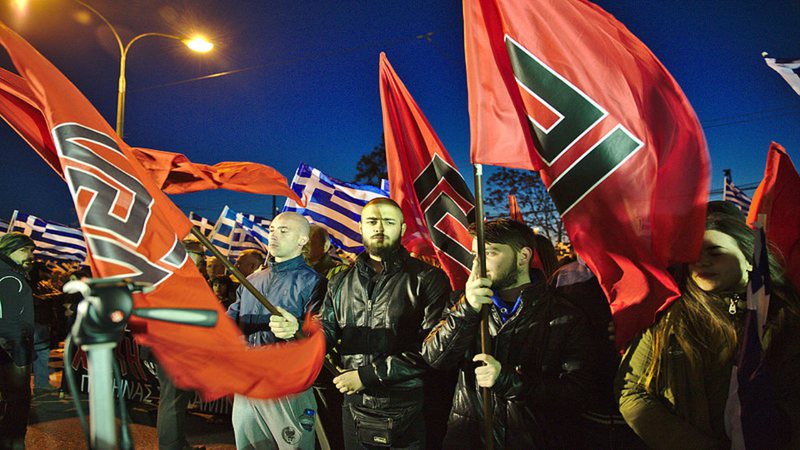 Membros da Golden Dawn seguram bandeiras com o símbolo do partido em comício de março de 2015 - Wikimedia Commons
