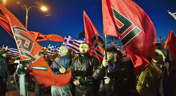 Membros da Golden Dawn seguram bandeiras com o símbolo do partido em comício de março de 2015 - Wikimedia Commons