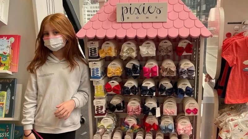 Pixie posa ao lado de gôndola contendo produtos de sua marca