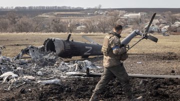 Membro do exército ucraniano passa pelos restos de helicóptero russo; a poluição causada pela guerra tem forte impacto ambiental - Chris McGrath/Getty Images