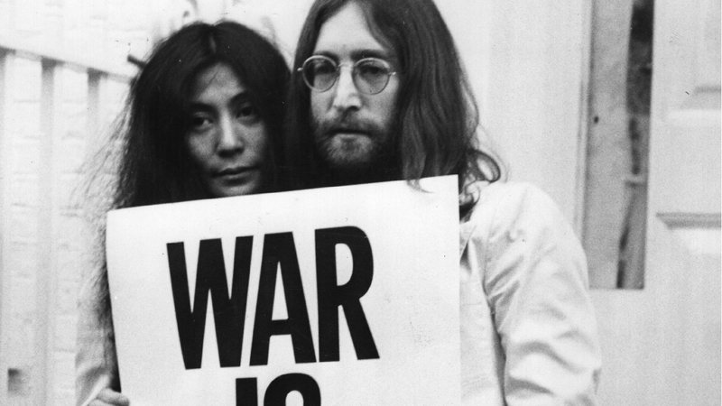 Yoko Ono e John Lennon com cartaz pedindo a paz - Getty Images
