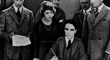 Chaplin sentado e assinando o documento da fundação da United Artists - Wikimedia Commons