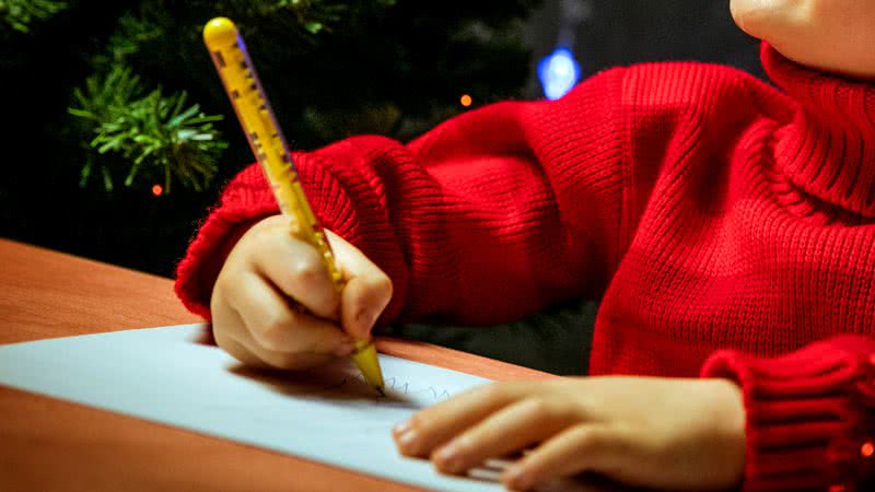 Imagem ilustrativa de uma criança escrevendo cartão de natal - Getty Images