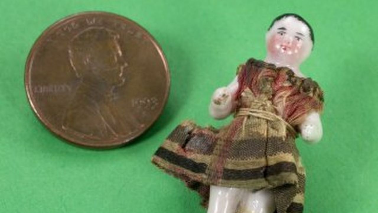 A boneca Frozen Charlotte sendo comparada com uma moeda